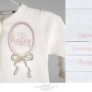 May include: A white baby onesie with a pink and white embroidered frame with the name "hailey" inside. The frame is decorated with a bow.