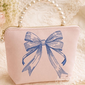 May include: A light pink fabric pouch featuring a blue embroidered bow design on the front. The pouch has a gold-toned zip closure and a top handle constructed from a single row of white faux pearls. The text Jaxton and Jill is visible.