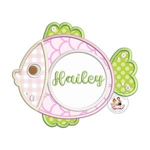 May include: A pink and green fish-shaped embroidery design with a white circle in the centre. The circle has the name "Hailey" written in green cursive.
