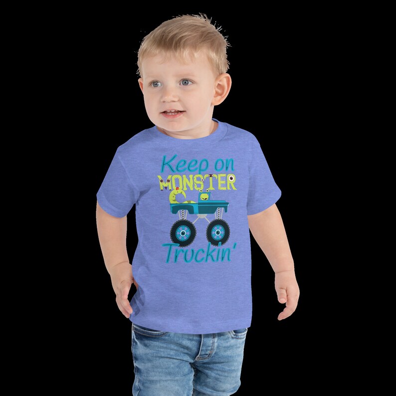 K&ouml;nnte beinhalten: Ein Kleinkind tr&auml;gt ein blaues T-Shirt mit kurzen &Auml;rmeln, auf dem ein gr&uuml;ner Monstertruck mit dem Text "Keep on Monster Truckin'" abgebildet ist.
