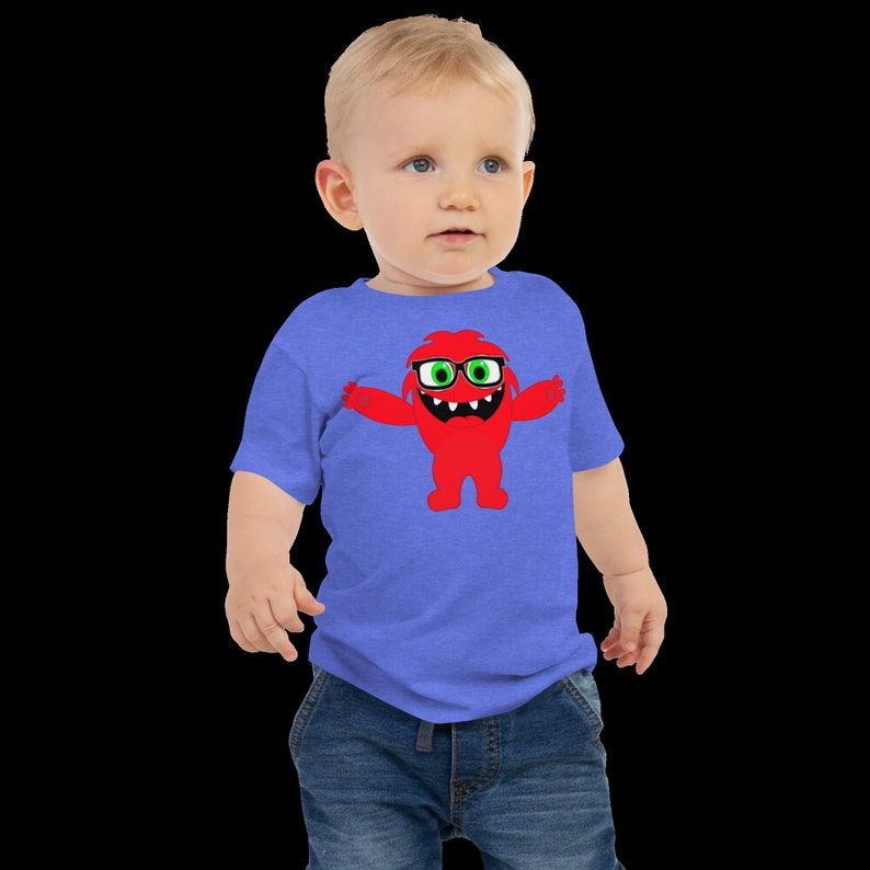 May include: A toddler wearing a blue heather t-shirt with a red monster graphic wearing green glasses. The monster is smiling and has its arms outstretched.
