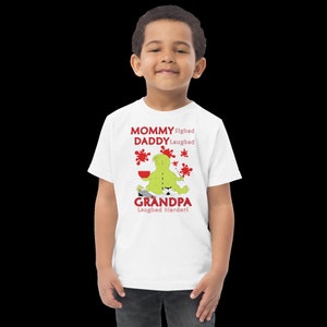 Puede incluir: Camiseta blanca con un personaje de dibujos animados verde pintando con salpicaduras de pintura roja. El texto en la camiseta dice "Mam&aacute; suspir&oacute;, pap&aacute; se ri&oacute;, &iexcl;abuelo se ri&oacute; m&aacute;s fuerte!"