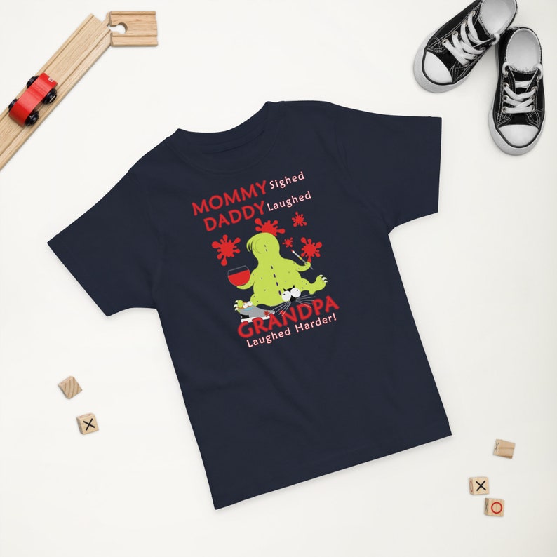 Puede incluir: Camiseta azul marino con un personaje de monstruo verde sosteniendo una copa de vino. El texto en la camiseta dice "Mommy sighed, Daddy laughed, Grandpa laughed harder!"
