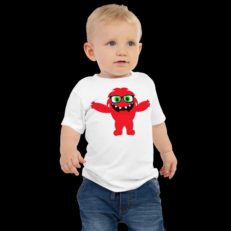 May include: A white toddler t-shirt with a red monster wearing glasses graphic. The monster has green eyes and a big smile.