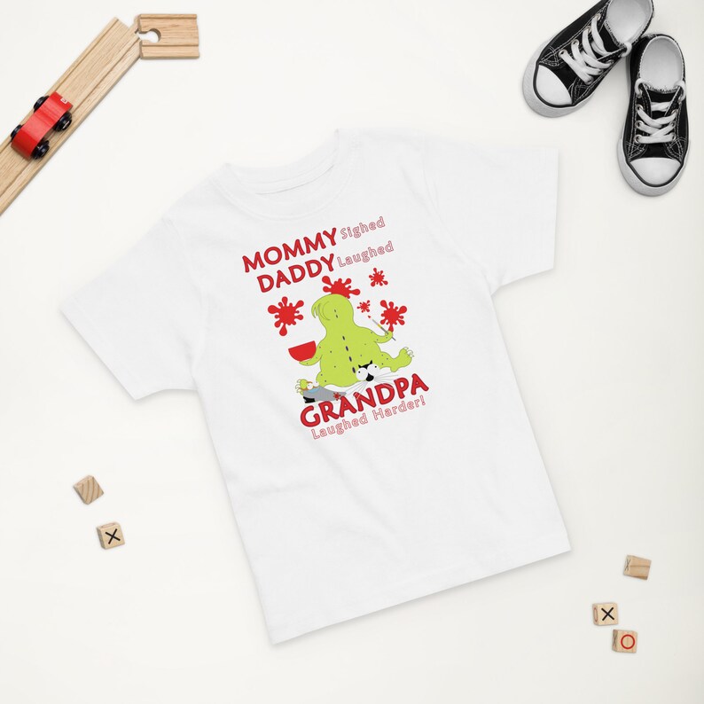 Puede incluir: Camiseta blanca con una ilustraci&oacute;n de un monstruo verde y el texto "Mommy sighed, Daddy laughed, Grandpa laughed harder!"