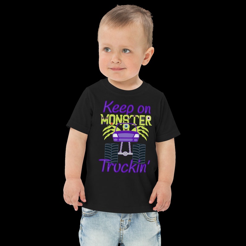 May include: A black toddler t-shirt with a purple and yellow monster truck graphic and the text "Keep on Monster Truckin'" printed on the front.