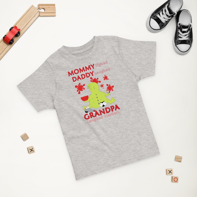 Puede incluir: Camiseta gris de manga corta con un gr&aacute;fico de monstruo verde y texto rojo que dice "Mam&aacute; suspir&oacute;, pap&aacute; se ri&oacute;, &iexcl;abuelo se ri&oacute; m&aacute;s fuerte!"