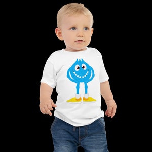 K&ouml;nnte beinhalten: Ein wei&szlig;es Baby-T-Shirt mit einem blauen Comic-Monster, das gelbe Schuhe tr&auml;gt. Das Monster hat ein breites L&auml;cheln und zwei Augen.