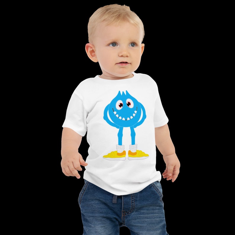 K&ouml;nnte beinhalten: Ein wei&szlig;es Baby-T-Shirt mit einem blauen Comic-Monster, das gelbe Schuhe tr&auml;gt. Das Monster hat ein breites L&auml;cheln und zwei Augen.