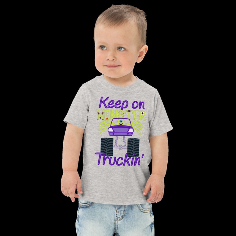 May include: A grey short-sleeved t-shirt with a purple and green monster truck graphic. The text "Keep on Monster Truckin'" is printed on the shirt.