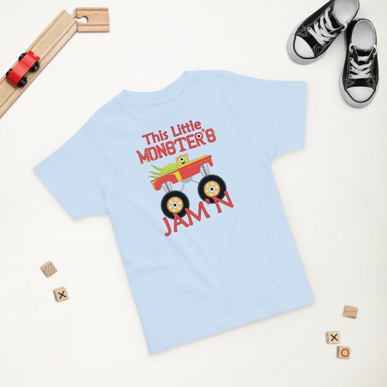 May include: Light blue short-sleeved t-shirt with a red monster truck graphic and the text "This Little Monster's Jam'n".