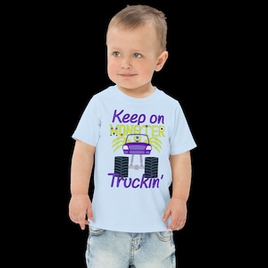 May include: A light blue toddler t-shirt with a purple and green monster truck graphic. The text "Keep on Monster Truckin'" is printed on the shirt.