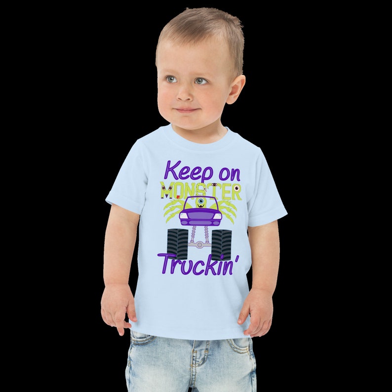 May include: A light blue toddler t-shirt with a purple and green monster truck graphic. The text "Keep on Monster Truckin'" is printed on the shirt.