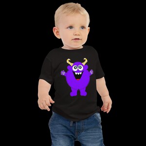 以下が含まれることがあります： 紫色のモンスターのグラフィックがプリントされた黒いTシャツを着た幼児。モンスターは黄色い角と大きな笑顔をしています。