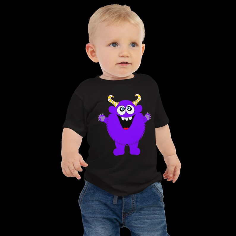 以下が含まれることがあります： 紫色のモンスターのグラフィックがプリントされた黒いTシャツを着た幼児。モンスターは黄色い角と大きな笑顔をしています。