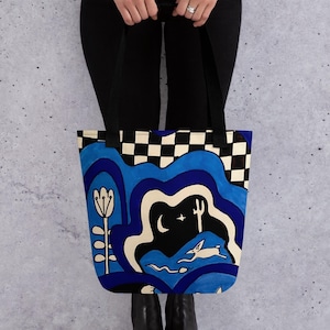 May include: A blue and white tote bag with a checkered pattern and a whimsical illustration of a rabbit running through a landscape with a crescent moon and stars.