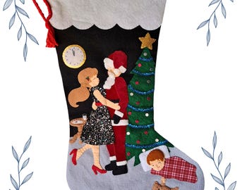 May include: A Christmas stocking with a black background and a grey cuff. The stocking features a felt design of a couple embracing, a Christmas tree, a clock, and a child sleeping. A red tassel hangs from the top.