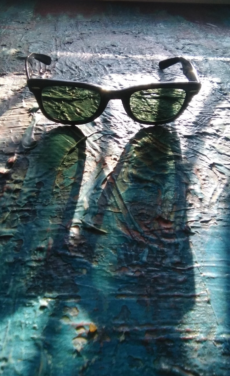 K&ouml;nnte beinhalten: Sonnenbrille mit schwarzem Rahmen und dunkelgr&uuml;n get&ouml;nten Gl&auml;sern. Der Rahmen hat eine klassische rechteckige Form mit abgerundeten Kanten und kleinen silberfarbenen Akzenten an den &auml;u&szlig;eren Ecken. Die B&uuml;gel sind schwarz und verlaufen gerade.