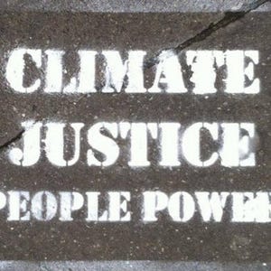 K&ouml;nnte beinhalten: Eine dunkelgraue, texturierte Oberfl&auml;che mit wei&szlig;em Schablonentext, der in der oberen Zeile CLIMATE JUSTICE und in der unteren Zeile PEOPLE POWER lautet. Ein d&uuml;nner, gezackter Riss verl&auml;uft diagonal &uuml;ber den oberen Teil der Oberfl&auml;che.
