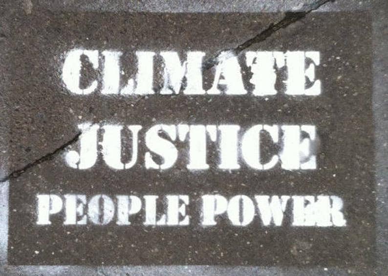K&ouml;nnte beinhalten: Eine dunkelgraue, texturierte Oberfl&auml;che mit wei&szlig;em Schablonentext, der in der oberen Zeile CLIMATE JUSTICE und in der unteren Zeile PEOPLE POWER lautet. Ein d&uuml;nner, gezackter Riss verl&auml;uft diagonal &uuml;ber den oberen Teil der Oberfl&auml;che.