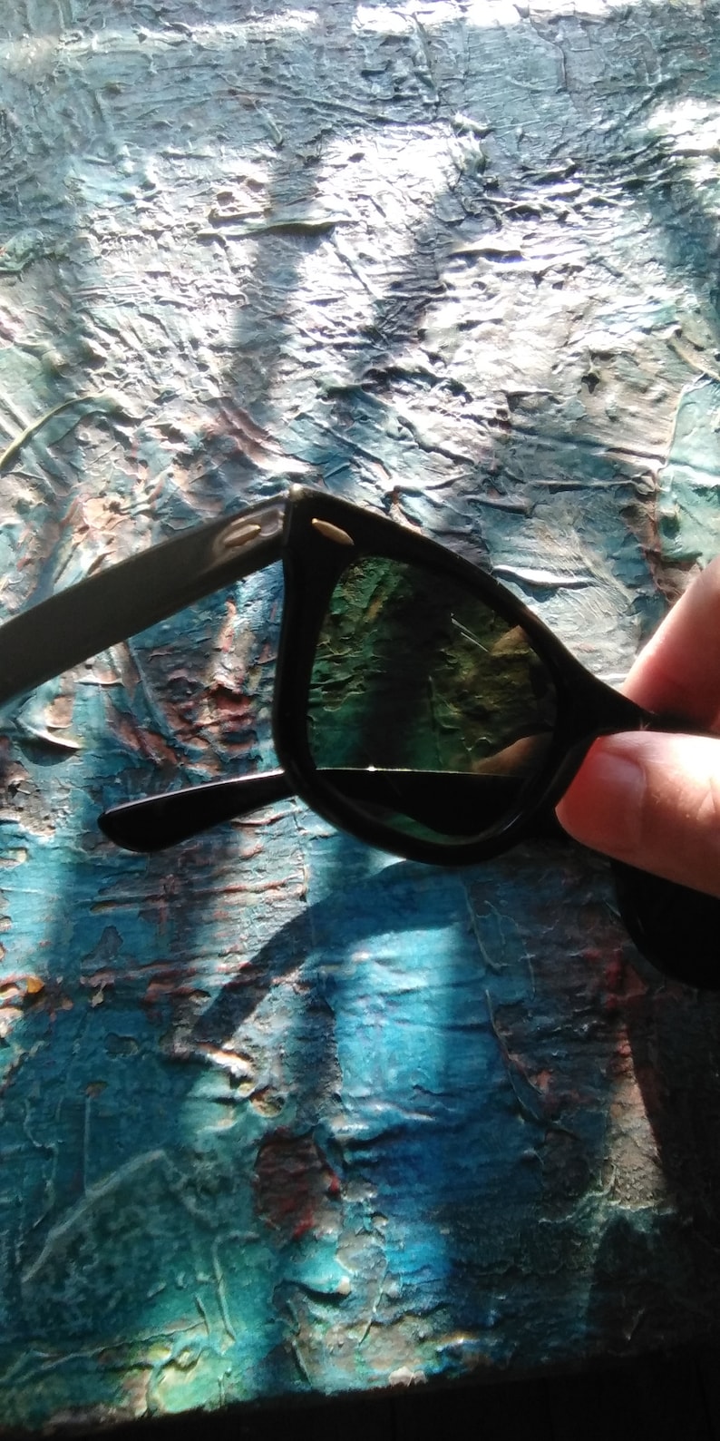 K&ouml;nnte beinhalten: Schwarze Sonnenbrille mit dunkel get&ouml;nten Gl&auml;sern und einem klassischen Rahmendesign. Die B&uuml;gel sind mit kleinen, metallisch silberfarbenen Akzenten an den Scharnieren mit dem Vorderrahmen verbunden, was dem dunklen Design ein dezentes Detail verleiht.