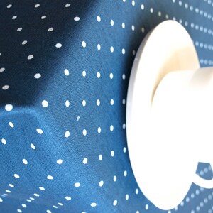 May include: A white teacup and saucer on a blue tablecloth with white polka dots.