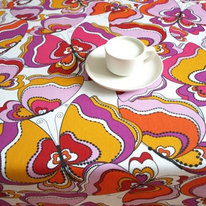 May include: A white tablecloth with a colorful butterfly pattern in shades of pink, orange, and yellow. The tablecloth features a stylized butterfly design with intricate details.