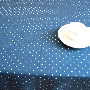 May include: A white saucer and cup on a blue tablecloth with white polka dots.