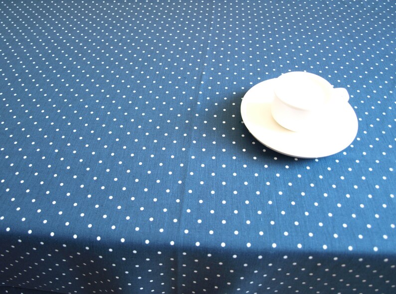 May include: A white saucer and cup on a blue tablecloth with white polka dots.