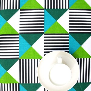 Puede incluir: Una taza y un platillo blancos sobre un mantel con un patrón geométrico de rayas blancas y negras, triángulos verdes y azules.