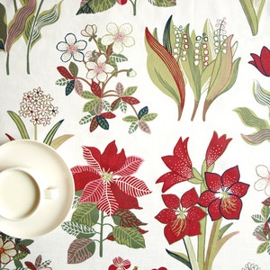 May include: A white tablecloth with a floral pattern featuring red, green, and white flowers. The tablecloth has a cup and saucer on it.