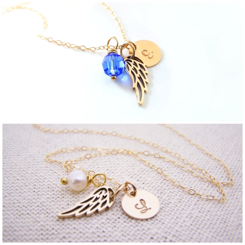 Puede incluir: Dos collares de oro con dijes de alas de &aacute;ngel. El collar superior tiene una cuenta de cristal azul y un dije redondo con la letra "S". El collar inferior tiene una cuenta de perla y un dije redondo con la letra "J".