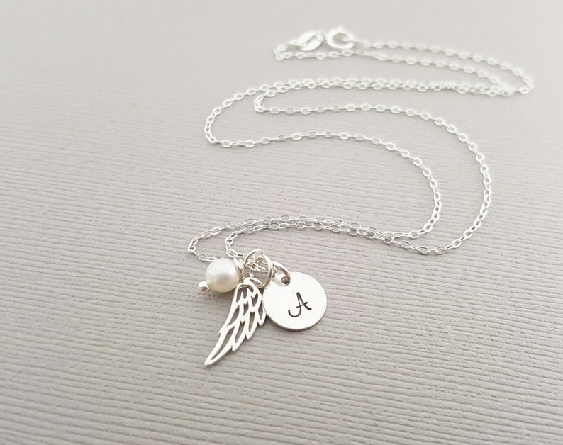 Puede incluir: Un collar de plata con un peque&ntilde;o dije de perla, un dije de ala de &aacute;ngel de plata y un dije de disco de plata con la letra 'A' grabada.