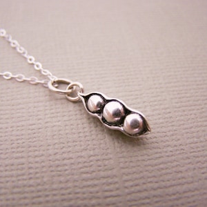 May include: A silver necklace featuring a pendant shaped like a pea pod with three peas. The pendant is attached to a delicate silver chain. The pea pod pendant is approximately 0.75 inches long.