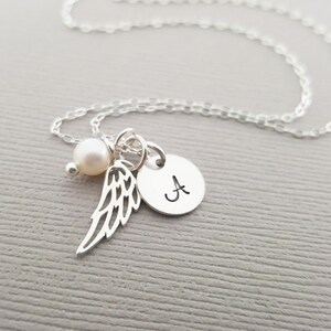Puede incluir: Collar de plata con un dije de perla, un peque&ntilde;o dije de ala de &aacute;ngel y un dije redondo con la letra 'A' grabada.