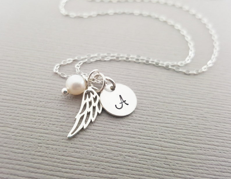 Puede incluir: Collar de plata con un dije de perla, un peque&ntilde;o dije de ala de &aacute;ngel y un dije redondo con la letra 'A' grabada.