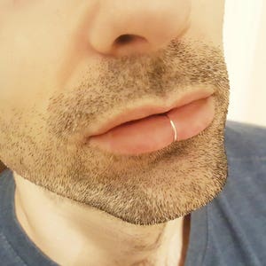 May include: A close-up of a person's lower face with a small silver ring piercing in their lower lip.