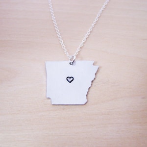 May include: A silver necklace with a pendant shaped like the state of Arkansas. The pendant has a small heart in the center.