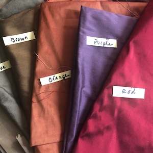 May include: A collection of fabric swatches in various colors, including brown, orange, purple, and red. Each swatch has a handwritten label with the corresponding color name.