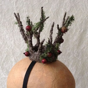 May include: A crown made of twigs, moss, and red berries. The crown is attached to a black headband.