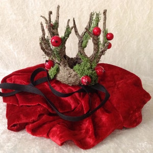 May include: A crown made of twigs and moss with red berries, resting on a red velvet surface.