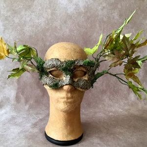 May include: A green and brown masquerade mask with moss and bark details, decorated with green and yellow leaves.