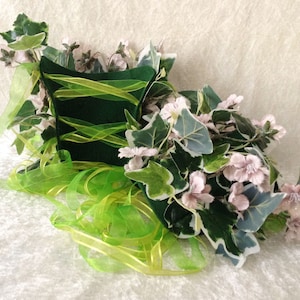 May include: A green felt hat with a green ribbon and pink flowers. The hat is decorated with green leaves and white flowers.