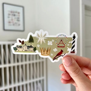 May include: A green outline of the state of North Carolina with various icons representing landmarks and symbols of the state. The icons include a pine tree, a white star, a crown, a Ferris wheel, a lighthouse, and a cardinal.
