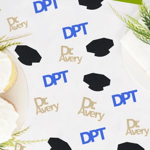 May include: White tablecloth with blue and gold glitter confetti. The confetti features the text "DPT" and "Dr. Avery".