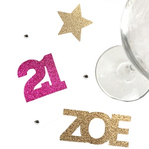 May include: Pink glitter number 21 and gold glitter letters spelling "ZOE" with a gold glitter star and a wine glass on a white background.