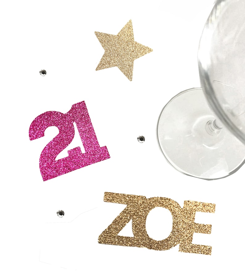 May include: Pink glitter number 21 and gold glitter letters spelling "ZOE" with a gold glitter star and a wine glass on a white background.