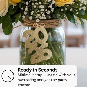 May include: A clear glass jar with a floral arrangement, featuring yellow roses and white baby's breath. A gold glitter "2020" ornament hangs in front. The jar is wrapped with twine. Text on the bottom reads "Ready in Seconds" and "Minimal setup - just tie with your own string and get the party started!!"