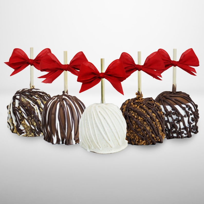 Puede incluir: Seis manzanas caramelizadas decoradas con lazos rojos. Las manzanas est&aacute;n ba&ntilde;adas en chocolate blanco, con leche y negro y cubiertas con diferentes ingredientes.