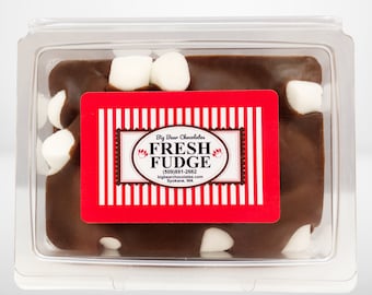 May include: A clear plastic container with a red and white striped label that reads "Big Bear Chocolates Fresh Fudge (509) 991-2662 bigbearchocolates.com Spokane, WA". The container holds a square of chocolate fudge topped with white marshmallows.